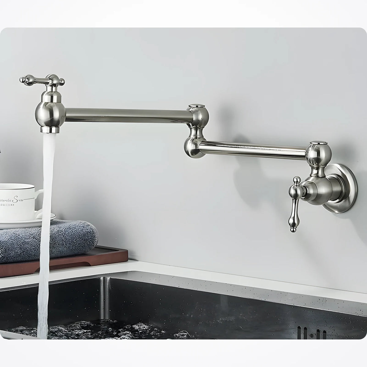 Robinet mural nickel à bras articulé fixé au-dessus d'un évier, jet d'eau froide qui coule, tasse et torchon posés à côté