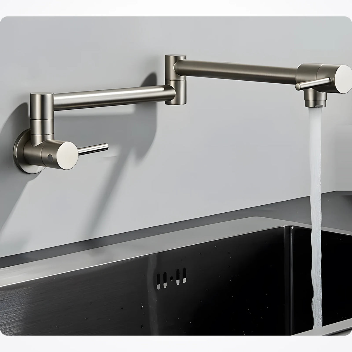 Robinet mural rabattable nickel brossé déplié au-dessus d'un évier en inox noir, jet d'eau froide ouvert