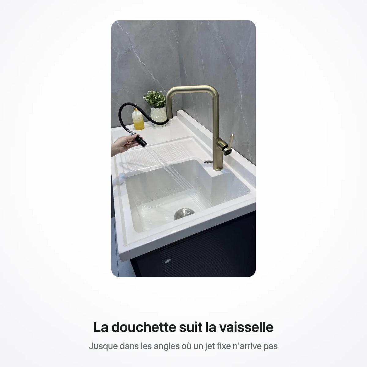 Main tirant la douchette du robinet doré au-dessus d'un évier blanc à deux bacs