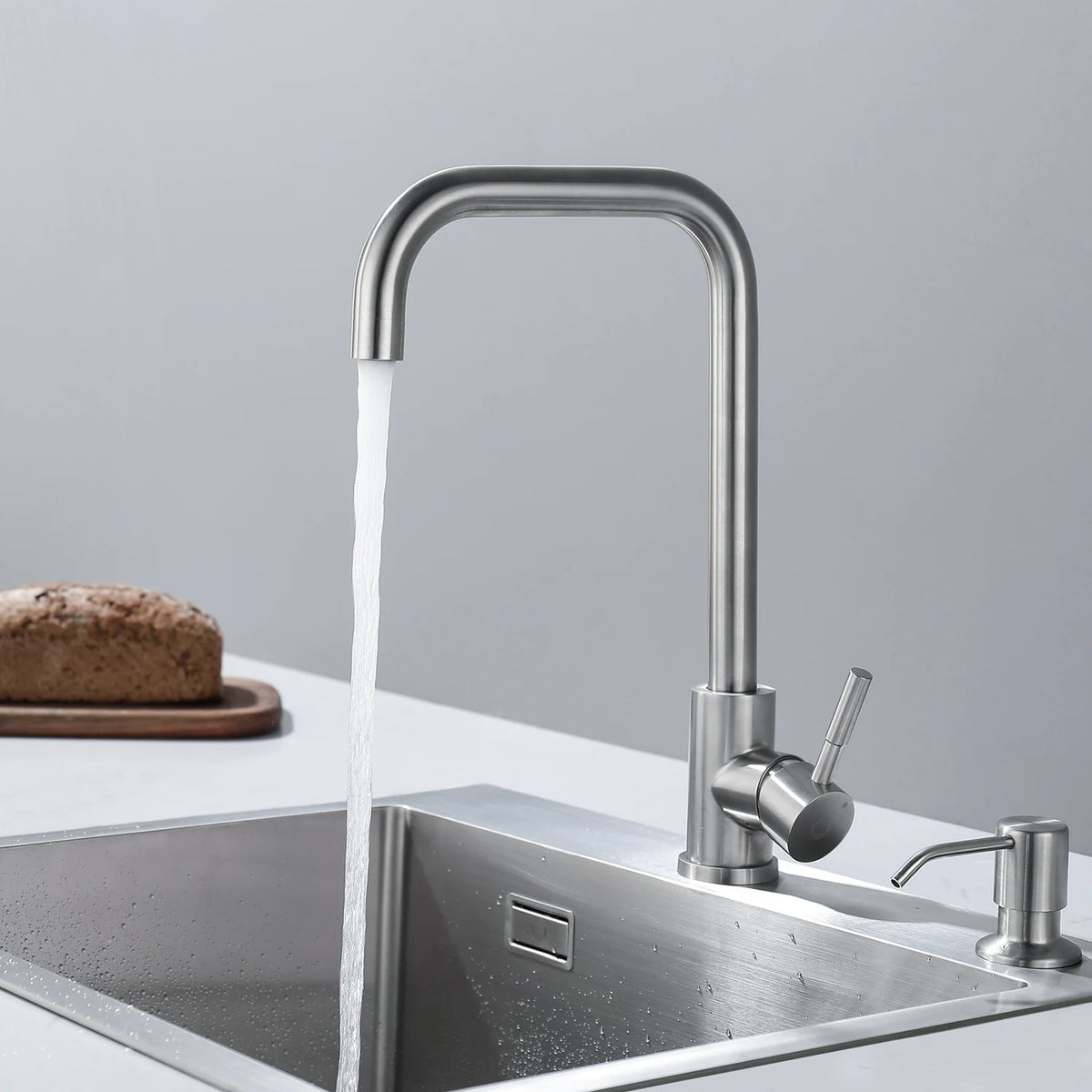 Robinet col de cygne installé sur un plan clair au-dessus d'un évier en inox, eau ouverte