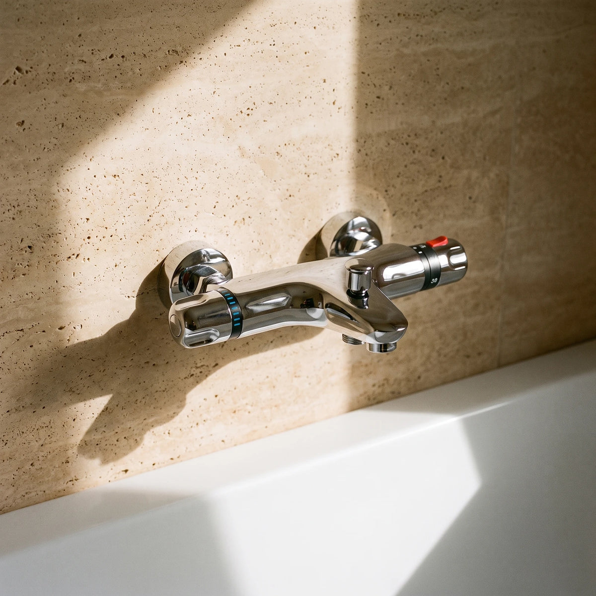 Robinet de baignoire thermostatique chromé sur un mur en travertin, au-dessus d'une baignoire blanche