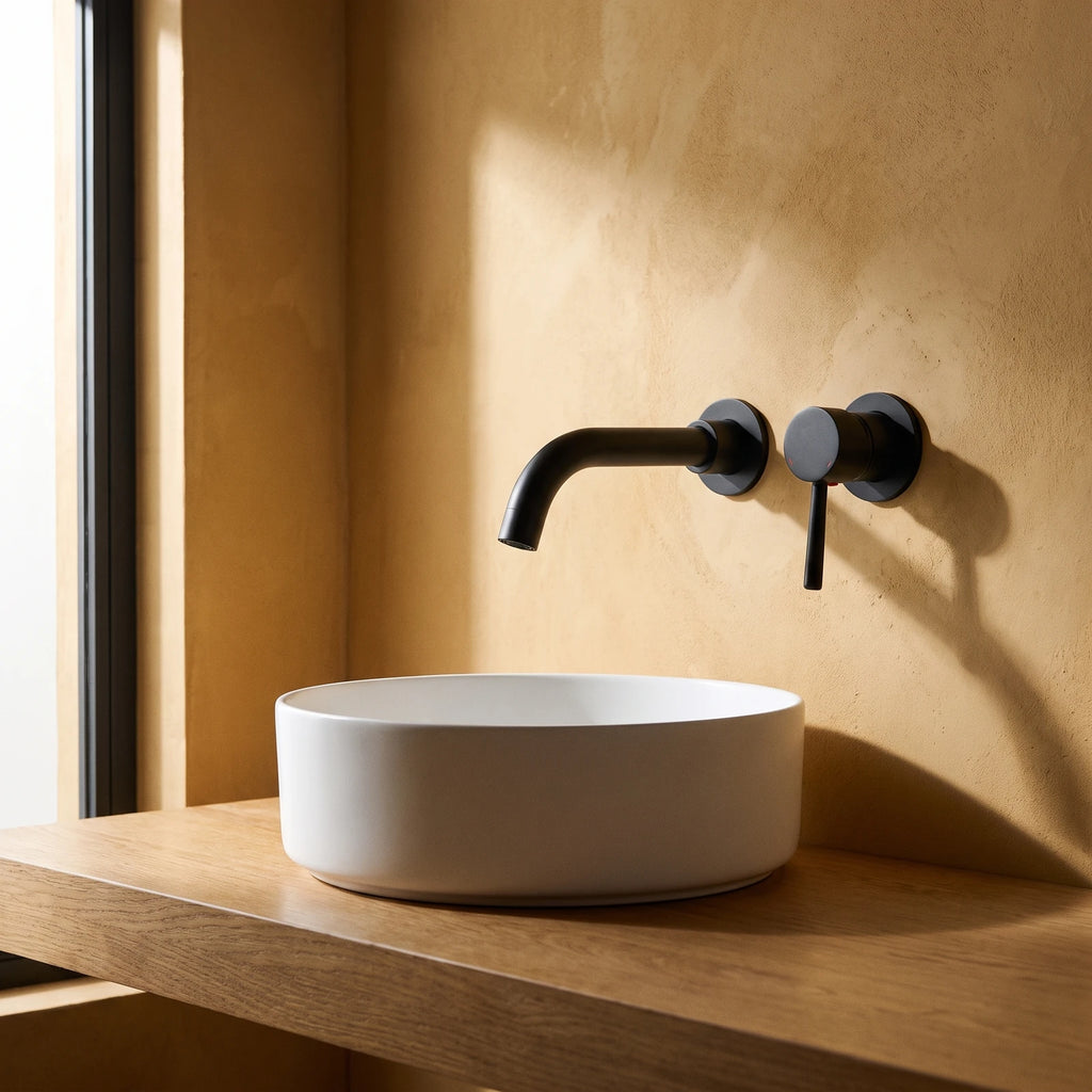 Robinet encastrable de lavabo noir mat sur un mur en enduit ocre, au-dessus d'une vasque ronde blanche posée sur un plan en chêne