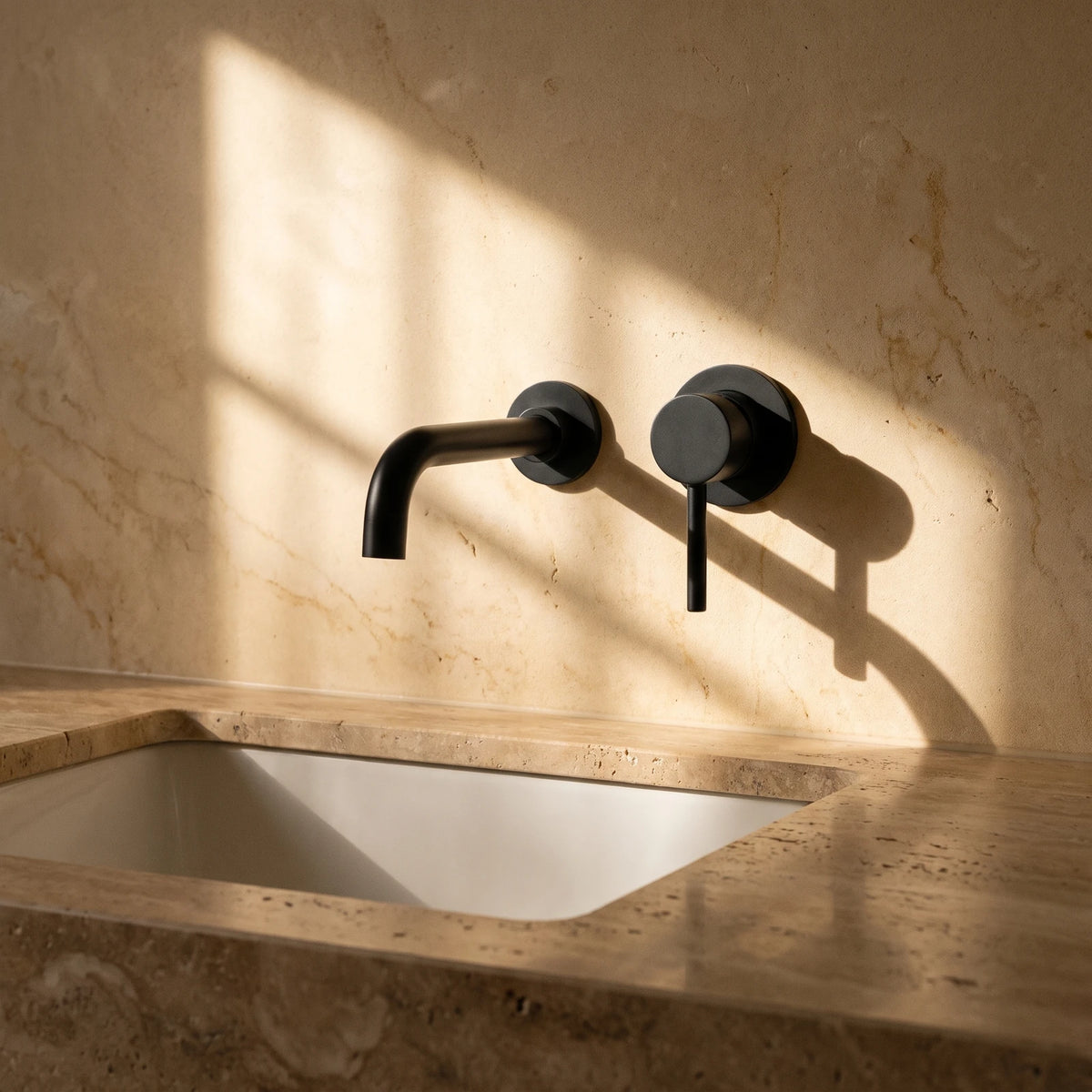 Robinet de lavabo mural noir mat, bec et commande séparés sur un mur de pierre