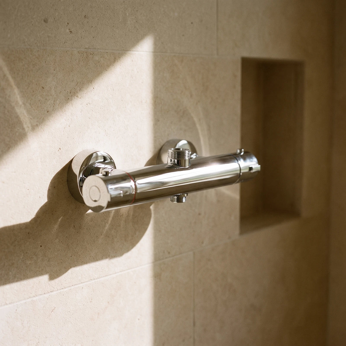 Robinet thermostatique de douche chromé sur un mur en pierre calcaire, près d'une niche