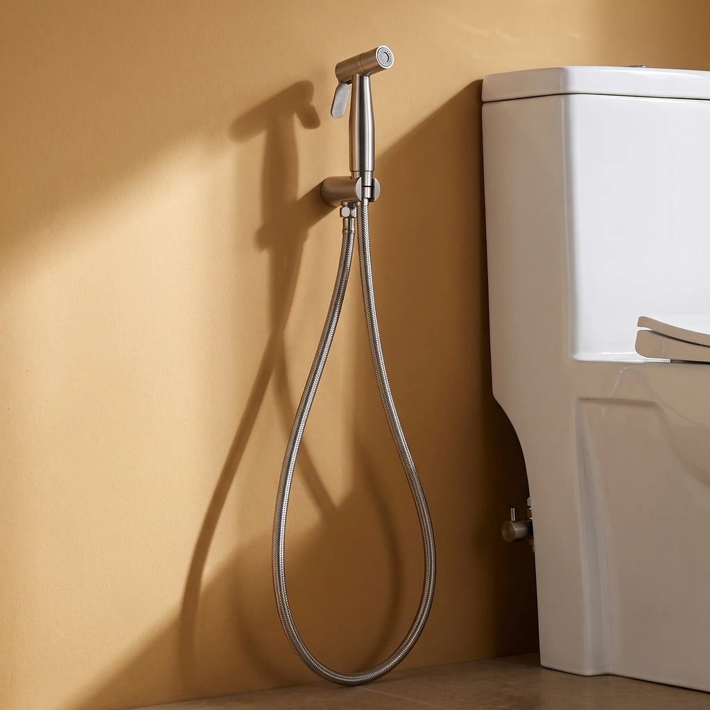 Douchette WC en inox sur son support mural, flexible descendant vers le robinet d'alimentation, mur en enduit ocre